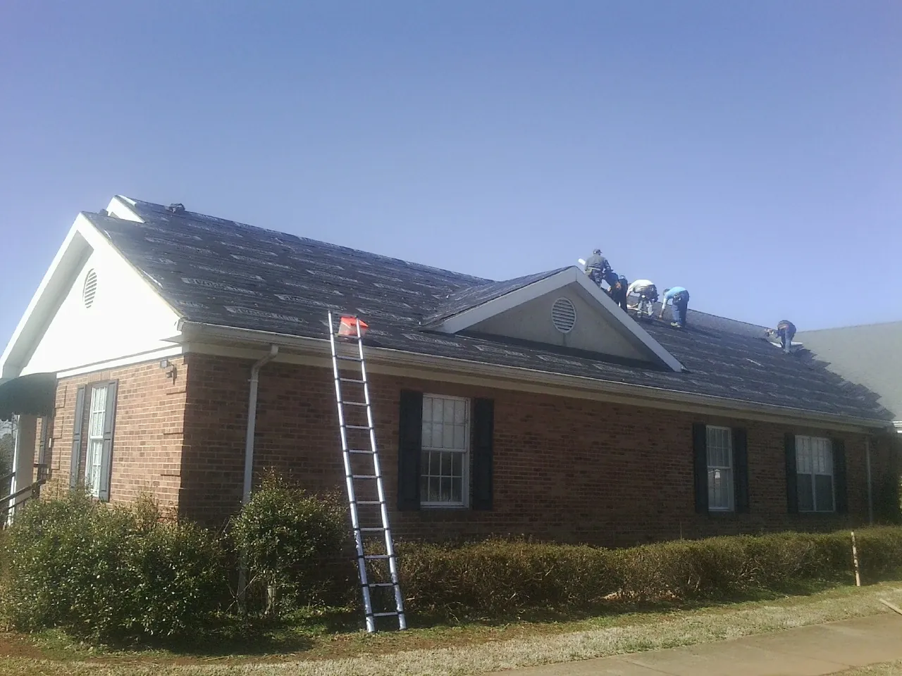 Crew tearing shingles off a brick ranch roof with a ladder set — Emergency Roof Repair work by our crew in Boston